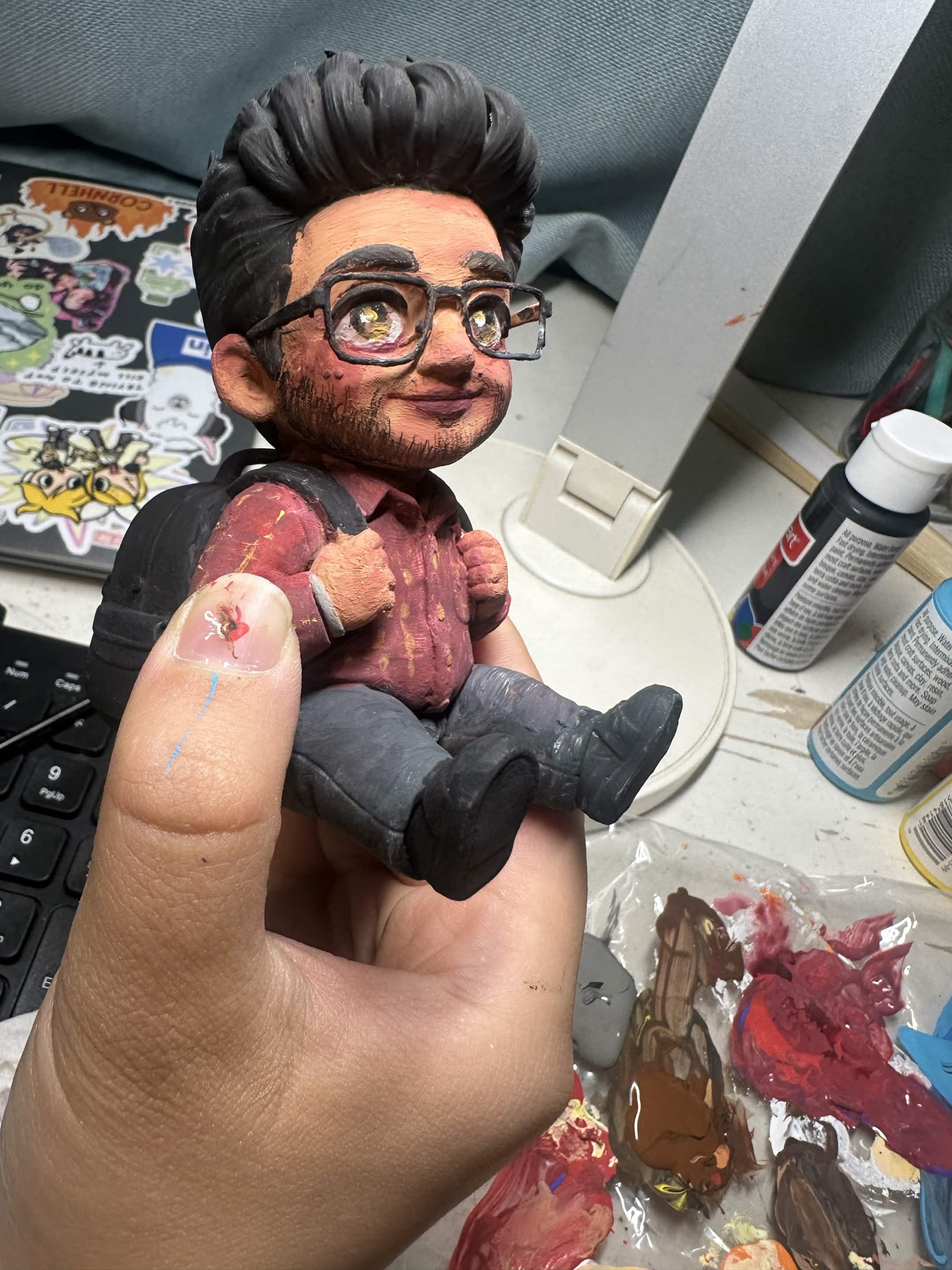 The figurine held in hand, hand-painted, above a palette of acrylic paint